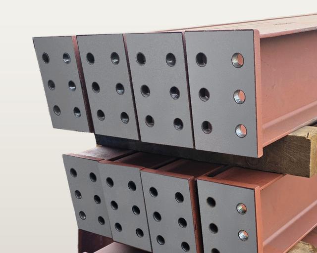 Close-up of steel end plates, each with six bolt holes, welded to the ends of painted beam pieces